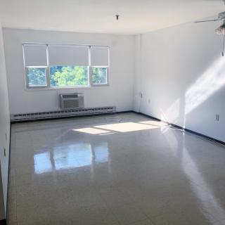 A bright, empty room with white walls and large windows allowing natural light in.
