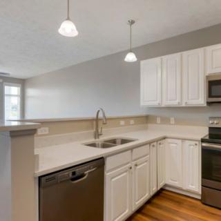 A modern kitchen featuring white cabinets, stainless steel appliances, and wooden flooring.