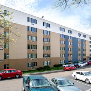 A view of a multistory residential apartment building with parking in front.