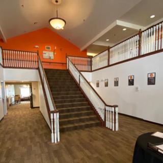 A spacious interior lobby featuring a central staircase with an orange accent wall and elegant lighting.