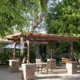 A wooden pergola with outdoor seating surrounded by lush greenery.