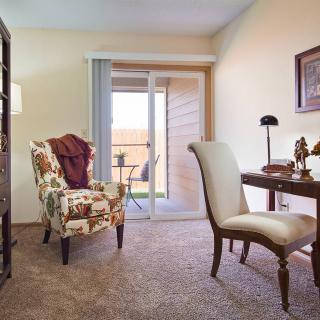 A cozy living room with a patterned armchair and elegant desk overlooking a balcony.