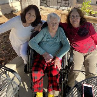 Three people enjoying time together outdoors, with one person seated in a wheelchair.