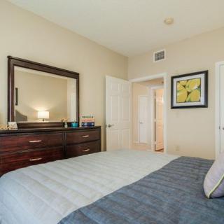A cozy bedroom with a neatly made bed, a large dresser topped with a mirror, and artwork on the walls.