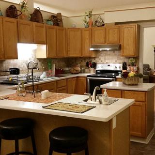 A modern kitchen with wooden cabinets, a central island with stools, and various appliances.