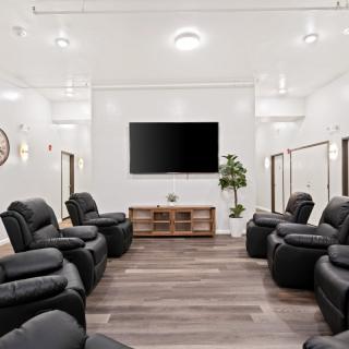 A modern living room with multiple recliners facing a large TV, featuring a minimalist design and hardwood flooring.