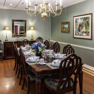 A formal dining room with a long wooden table set for a meal, featuring elegant chairs, a chandelier, and decorative wall art.