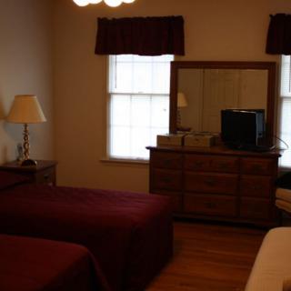 A cozy bedroom with twin beds, a dresser with a mirror, and a lamp by the window.