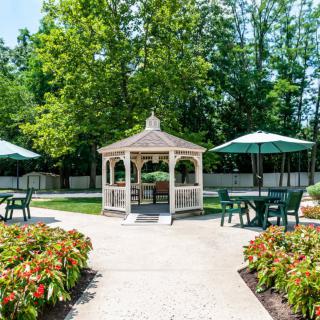 A peaceful garden with a central gazebo and surrounding tables with umbrellas.