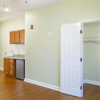 A small kitchenette in an apartment with wood flooring, featuring a closet and cabinets.