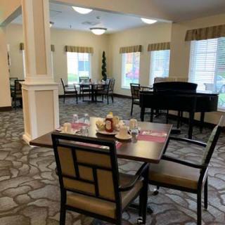 A well-lit dining area with neatly set tables and a piano in the background.