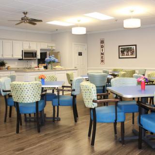 A modern dining area with a kitchen, featuring colorful chairs and tables in a community setting.