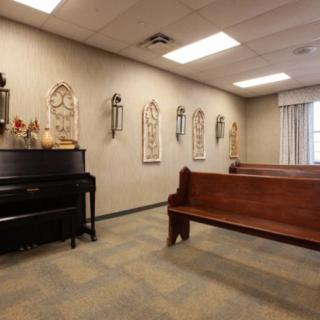 A small chapel with wooden pews, a piano, and religious decorations on the wall.