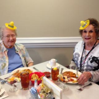 Two seniors enjoying a meal together, wearing playful yellow hats.