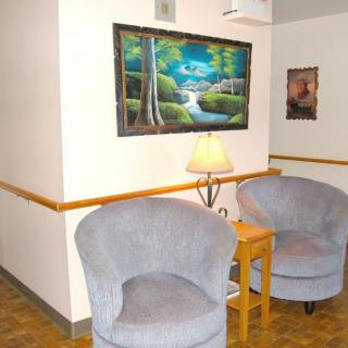 A cozy corner with two chairs, a small table, and a lamp under a scenic painting.