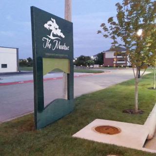 A roadside sign with a tree logo near a building during the evening.