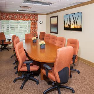 A well-furnished conference room with an oval meeting table and comfortable office chairs, featuring artwork on the wall.
