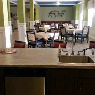 A neatly arranged dining area with multiple tables and chairs, viewed from behind a countertop with a sink.