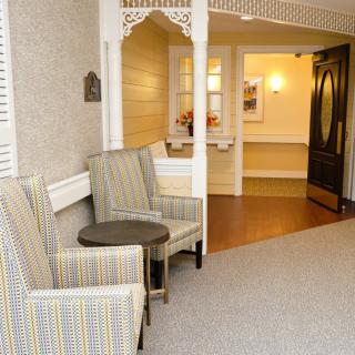 A cozy lobby area with patterned chairs and a small table, leading to a well-lit hallway.