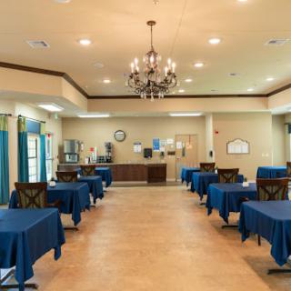 A spacious dining area featuring tables draped in blue tablecloths, illuminated by a chandelier.