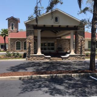 A charming building featuring a combination of stone and modern architectural elements, surrounded by trees and a well-maintained parking area.