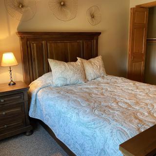 A cozy bedroom with a wooden bed frame, nightstand, and a lit lamp.