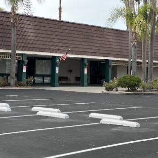 A view of a commercial building with a spacious parking lot and palm trees.