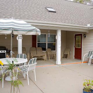 A cozy outdoor patio with chairs, tables, and an umbrella, situated next to a house.