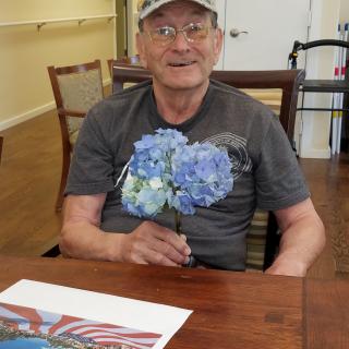 A man sitting at a table holding blue flowers and smiling.