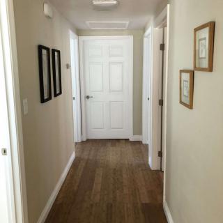 A bright hallway with wooden floors and artwork on the walls, featuring several doors.