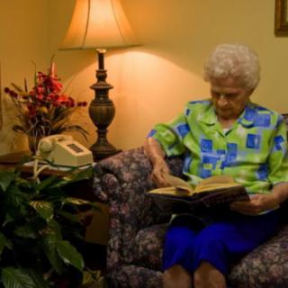 An elderly woman reading a book in a cozy living room setting.