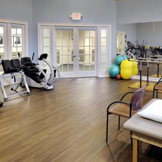 A spacious gym room with exercise equipment, therapy balls, and mirrors.