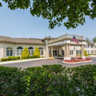 A sunny view of a building entrance with well-maintained landscaping and an American flag.