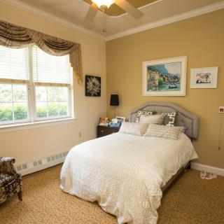 A cozy bedroom with a neatly made bed, decorated with artwork and soft lighting.