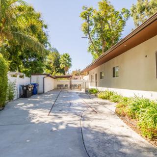 A sunny driveway leading to a house, surrounded by trees and landscaping.