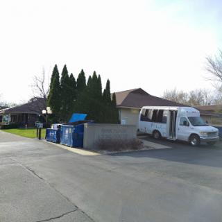 A white van parked near a dumpster surrounded by tall trees in a residential area.