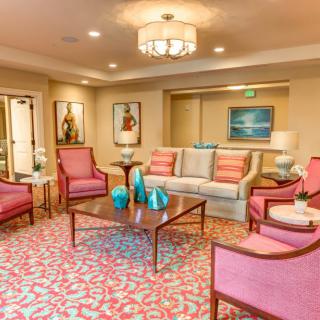 A cozy living room with pink chairs and a patterned rug, accented by modern artwork and elegant lighting.