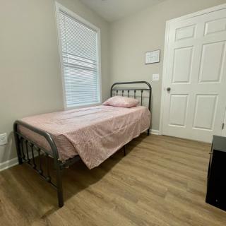 A simple bedroom with a single metal-framed bed and pink bedding, featuring a window and wooden flooring.