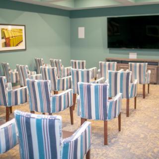 A conference room with striped upholstered chairs arranged facing a large television.
