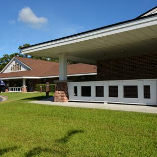 A modern building with a sloped roof and brick accents surrounded by green grass under a clear blue sky.