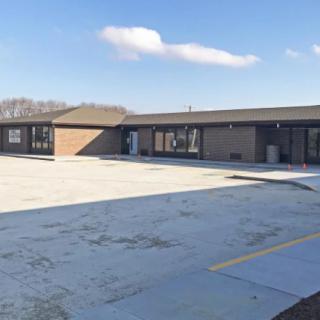 A wide view of a single-story building with an empty parking lot under a blue sky.