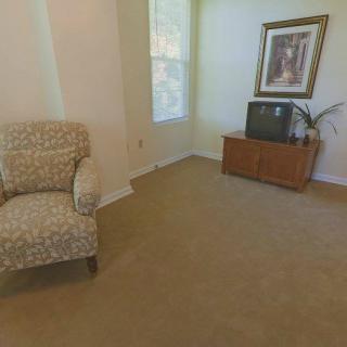 A cozy living room with a patterned chair, a TV on a wooden stand, and a decorative painting.
