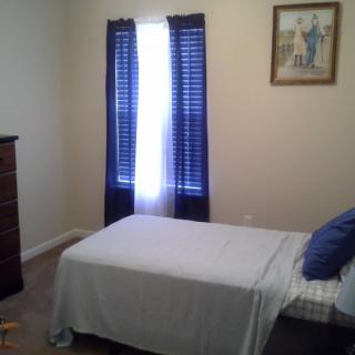 A simple bedroom with a single bed, blue curtains, and a dresser.