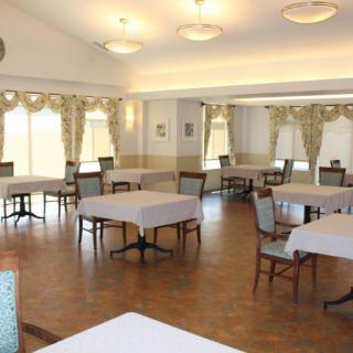 An empty dining room with neatly arranged tables and chairs, decorated with curtains and lit by overhead lights.