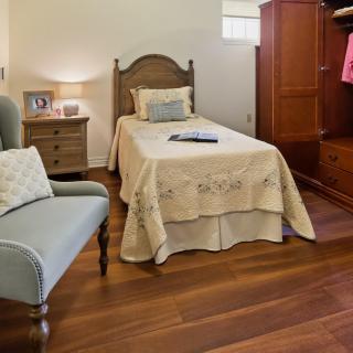 A cozy bedroom with a single bed and wooden flooring, featuring a nightstand and an armchair.