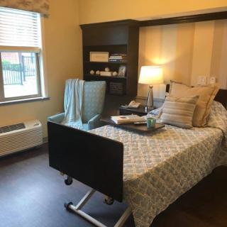 A cozy hospital room featuring a bed, sitting area, and warm lighting.