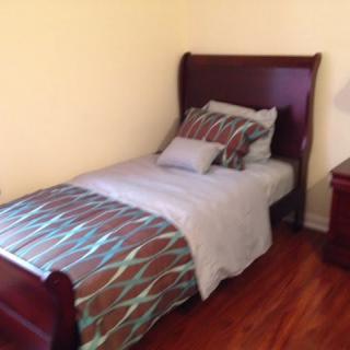 A simple bedroom setup featuring a single bed with patterned bedding, a wooden floor, and a nightstand.