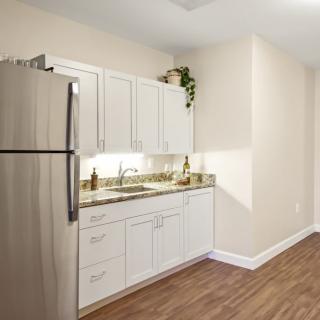 A modern kitchen featuring white cabinets and a stainless steel refrigerator with wood flooring.