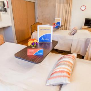 A cozy hotel room featuring twin beds with a side table, decorated with pillows and equipped with a television.