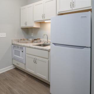 A compact kitchen with white cabinets, a refrigerator, microwave, and a sink.